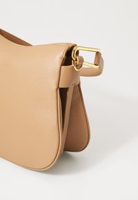 Borsa in pelle marrone chiaro con finitura testurizzata, dotata di una fibbia in hardware dorato, chiusura a zip e una forma strutturata. Design minimalista.