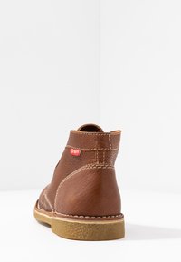 Bottine en cuir marron avec surface texturée, couture contrastante et étiquette de logo rouge. Bout arrondi et semelle en caoutchouc pour une meilleure traction.