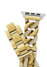 Złota metalowa bransoletka z dużymi ogniwami połączonymi ze sobą, ozdobiona przezroczystymi cyrkoniami. Posiada wygrawerowane logo "GUESS" oraz srebrną zapięcie.