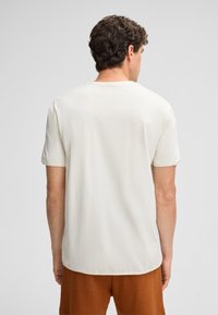 Kurzärmliges T-Shirt mit Rundhalsausschnitt aus off-white Baumwolle. Hat einen lockeren Schnitt und einen geraden Saum mit dezenten Nähdetails.
