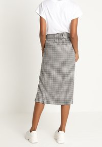 Falda midi de cuadros en blanco y negro con cintura elástica, combinada con una camiseta blanca básica y zapatillas blancas gruesas.