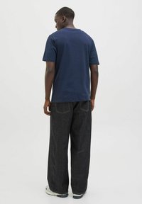 Marineblå bomulds t-shirt med korte ærmer, parret med løstsiddende, mørk denimbukser med synlige syninger og to baglommer.