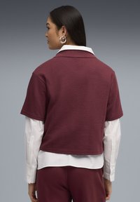 Maglietta a maniche corte di colore marrone scuro con una finitura strutturata, che presenta una camicia bianca con colletto sotto e una vestibilità comoda.