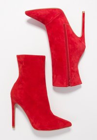 Stivaletti alla caviglia in suede rosso con punta affusolata, tacco a stiletto alto e chiusura con zip laterale. Texture liscia e silhouette elegante.