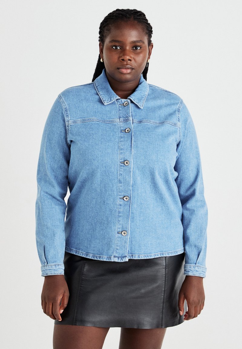 Gai zilā džinsu jaka ar pogu aizdari, norādītu apkakli un garām piedurknēm, kombinēta ar melnu ādas mini svārku.