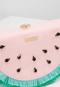 Clutch in ecopelle rosa con decorazioni a goccia nera e un accento in frange verdi. Dotato di hardware dorato e dettaglio del logo in rilievo.