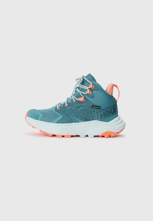 Teal turistsko sko med mesh-overdel, oransje detaljer og reflekterende snørebånd. Har en polstret såle og en Vibram-yttersåle for godt grep.