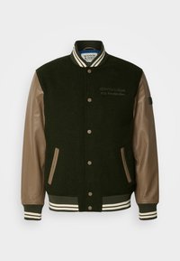 Chaqueta varsity de mezcla de lana verde con mangas de cuero marrón, cuello de canalé a rayas y cierres de botón. Cuenta con bolsillos laterales y bordado del logotipo.