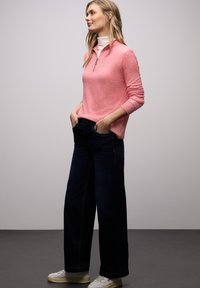 Jasnoróżowy pulower z kołnierzem na zamek, zestawiony z szerokimi granatowymi dżinsami i białymi trampkami. Gładka faktura, casualowy design.