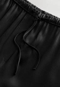 Sort elastisk linning med snor, der har en glat tekstur og letvægtsstof. Nærbillede, der fremhæver stoffets glans.