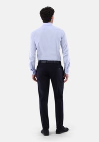 Hellblaues Langarmhemd mit Manschettenknöpfen, kombiniert mit dunkelblauen Hosen. Glatter Stoff und maßgeschneiderte Passform betonen das moderne Design.