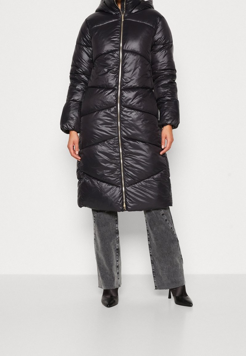 Manteau long matelassé en noir brillant avec une capuche, présentant un design matelassé diagonal, une fermeture éclair avant et des poignets côtelés ajustés.