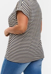 Námořnická a krémová pruhovaná krátká tričko s volným střihem, se zaobleným výstřihem a zakřiveným lemem. Nosené s modrými džíny.