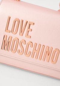 Bolsa em pele sintética rosa com o texto em relevo, metálico, cor rosa dourado "LOVE MOSCHINO" na parte da frente, com textura suave e detalhes cosidos.