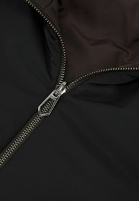 Schwarzes Jackenfutter mit braunem Innenfutter, ausgestattet mit einem silbernen Reißverschluss und fein gearbeiteten Nähten entlang der Reißverschlusskanten.