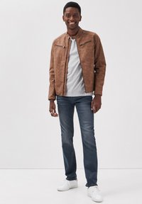 Brązowa kurtka z materiału skóropodobnego z zamykanymi kieszeniami, w połączeniu z jasnoszarym t-shirtem, niebieskimi dżinsami i białymi sneakersami. Prosty design, casualowy krój.