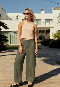 Bež cropped top, rohelised laiad cargo püksid nupuga kinnitusega ja küljetaskutega, pruunid toonilised prillid, mustad sandaalid. Väljas keskkond.