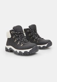 Melni pārgājienu apavi ar baltu kažoku, ar metāla āķiem, pelēkām un melnām shoelaces, teksturētu melnu zoli un biezu balto starpzoli.