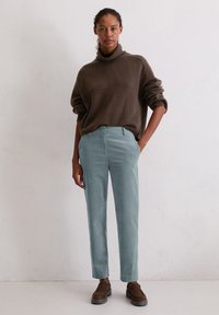 Bruine, chunky coltrui gecombineerd met lichtblauwe, op maat gemaakte broek, met een soepele textuur en een ontspannen pasvorm. Bruine schoenen maken de outfit af.