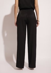 Czarne spodnie z szerokimi nogawkami, o gładkiej fakturze, z średnim stanem i bez wyróżniających się wzorów czy detali metalowych.