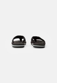 Tongs noires avec une semelle plate dotée d'un fond texturé et de deux brides. Des accents blancs sur la semelle offrent un contraste.