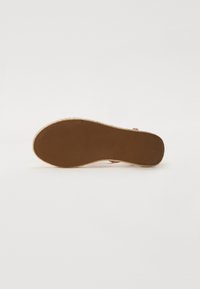Semelle en caoutchouc marron avec texture rainurée, présentant un bord en jute tissé. Forme plate et ronde sans marque ni motifs visibles.