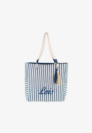 Bolsa tote a rayas en azul y blanco con asa de cuerda, con un tassel y la palabra "La's" en cursiva. Material de algodón texturizado.