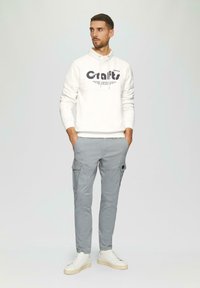 Witte sweatshirt met een grafische print, grijze cargobroek met zijzakken en witte lage sneakers. Glad materiaal en casual pasvorm.