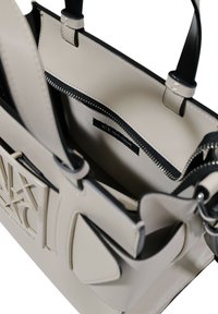 Borsa tote in materiale sintetico beige con accenti neri, dotata di una tasca con zip, manici e logo in rilievo sul davanti.