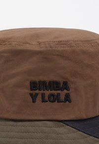 Sombrero de cubo marrón con diseño reversible en verde oliva y azul marino. Logo bordado "BIMBA Y LOLA" en negro en la parte delantera.