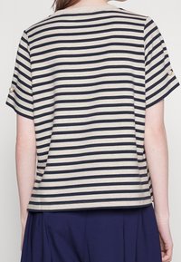 Top de manga corta a rayas en crema y azul marino, con botones en las mangas y un corte holgado. Textura suave con un ajuste relajado.