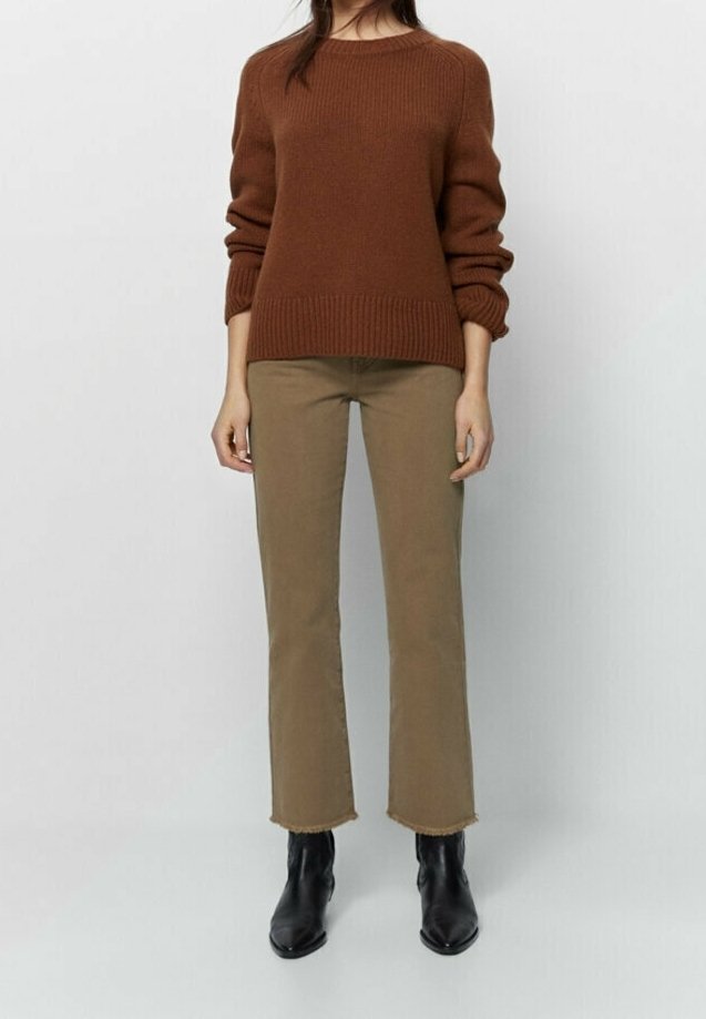 Pull en maille marron avec poignets côtelés, associé à un pantalon beige à ourlets effilochés et des bottines noires.