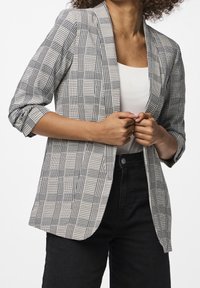 Krageblazer i ett svart-vitt rutmönster, med uppvikta trekvartsärmar och en lätt, strukturerad design.