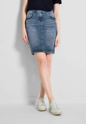 Denim skirt in light wash with a fitted silhouette, mid-thigh length, and visible front pockets. Paired with light-colored sneakers.