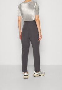 Chemise à manches courtes rayée gris et beige associée à un pantalon noir taille haute et des baskets blanches. Design minimaliste avec une coupe moderne.