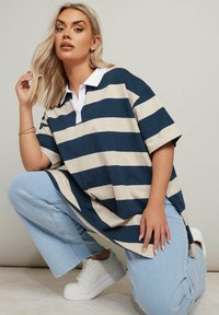 Randig polo skjorta i marinblått och beige, kortärmad, klassisk krage, matchad med ljusblå jeans och vita sneakers. Avslappnad look.