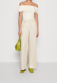 Krémový off-the-shoulder top, krémové široké kalhoty s vysokým pasem, zelená kabelka, odpovídající zelené loafers, minimalistic hardware detaily.