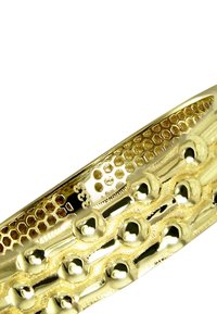 Bracelet manchette en or avec une surface texturée présentant des motifs hexagonaux et des accents arrondis. Finition lisse avec un aspect métallique brillant.