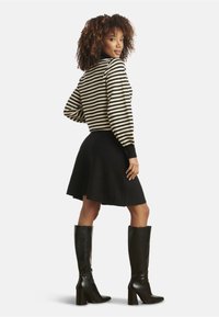 Gestreifter Strickpullover in Schwarz und Creme, kombiniert mit einem schwarzen ausgestellten Rock und knielangen schwarzen Stiefeln mit Absatz, was eine geschichtete Silhouette kreiert.