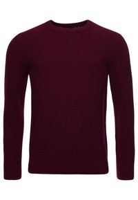 Pull en maille bordeaux avec un col rond, un motif texturé et des manches longues. Poignets et ourlet côtelés, avec un petit logo en accent.
