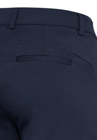 Vue arrière d'un pantalon bleu marine montrant la ceinture avec passants pour ceinture et une poche passepoilée unique sur le côté droit.