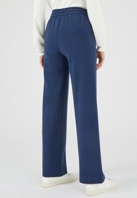 Marineblauwe trainingsbroek van textuurstof, met een elastische tailleband en brede pijpen. Draagt witte sneakers, wat het eenvoudige ontwerp en de casual pasvorm laat zien.