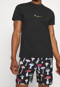 Black cotton t-shirt with short sleeves and yellow embroidered text. Paired with black shorts featuring a colorful mushroom print.