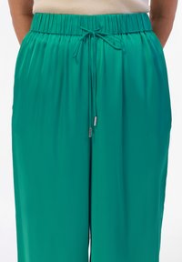 Teal wijde broek gemaakt van lichtgewicht materiaal, met een elastische tailleband voorzien van een trekkoord met metalen uiteinden voor verstelbaarheid.