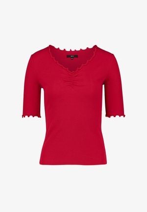 Piros, bordázott rövid ujjú felső hullámos szegélyekkel és enyhén gyűrt részlettel a nyakkivágás közepén.