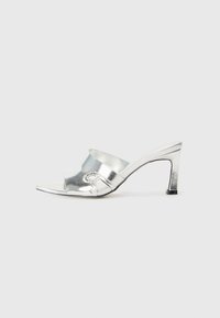 Zilveren hoge hak slide sandaal met een glanzende metallic afwerking, open teen en een gebogen bandontwerp, met een gestructureerd accent aan de zijkant.