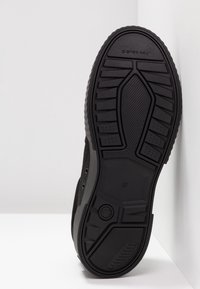 Semelle de chaussure noire avec des motifs de bande de roulement texturés, affichant la marque "G-STAR RAW" et la taille "37" sur une surface blanche.