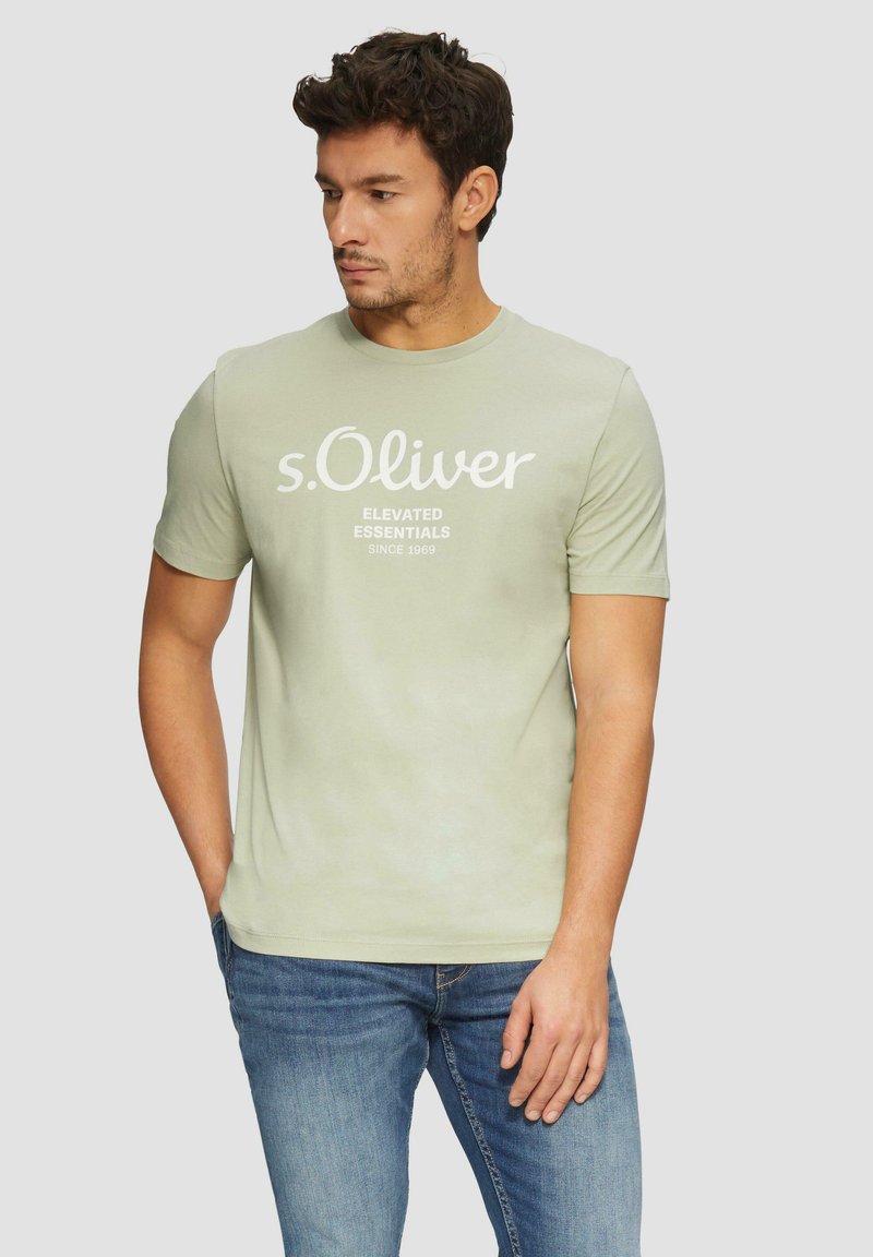 Kerge roheline puuvillane t-särk ümarate krae ja lühikeste varrukatega, ees valge tekstiga "s.Oliver ELEVATED ESSENTIALS SINCE 1969".