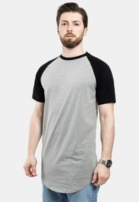Harmaa ja musta raglan-paita lyhyillä hihoilla, pyöreällä kauluksella ja kaartuvalla helmalla. Kangas näyttää pehmeältä ja sileäpintaiselta.