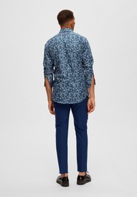 Mörkblå långärmad skjorta med blommönster, kombinerad med slim-fit blå byxor. Skjortan har krage och sidoflikar.